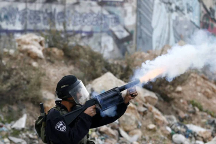 
	Um policial israelense dispara g&aacute;s lacrimog&ecirc;neo em manifestantes palestinos durante a opera&ccedil;&atilde;o militar de Israel na Faixa de Gaza: Israel bombardeou hoje cerca de 120 alvos
 (Marko Djurica/AFP)