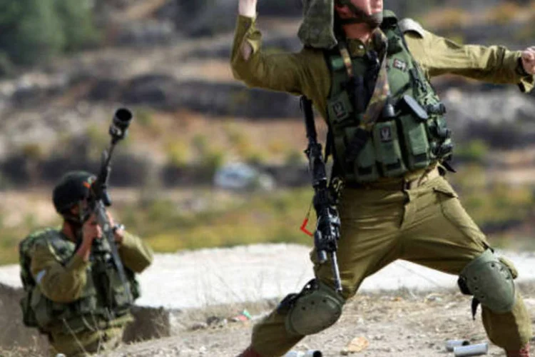 Soldado israelense lança granada contra manifestantes palestinos em Bet Omar, durante protesto contra operação militar israelense na Faixa de Gaza (ABED HASHLAMOUN/Lusa/ABr)