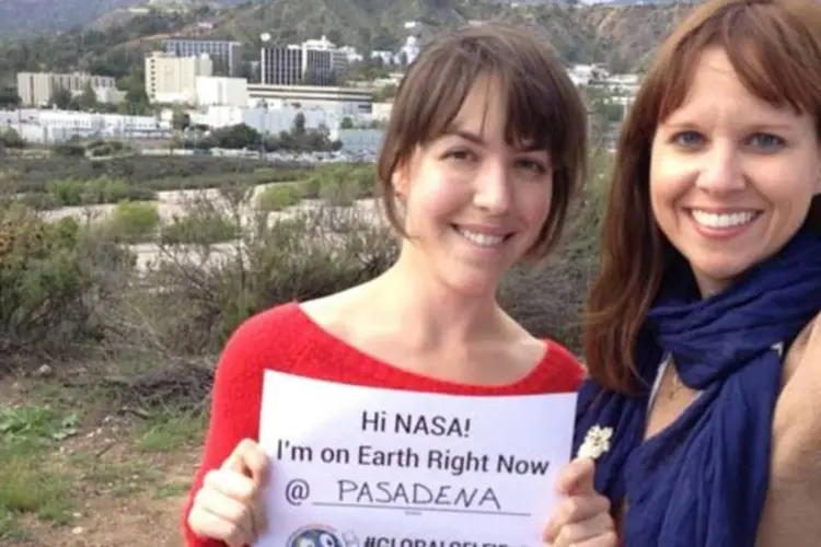 
	Mulheres posam com cartaz que promove selfie global pelo Dia da Terra 2014
 (Divulgação/NASA)