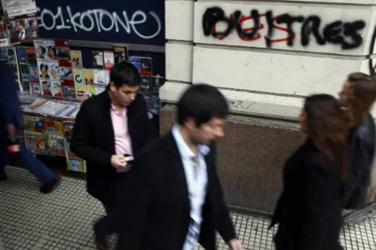 
	Pedestres caminham ao lado de grafite que diz &quot;Fora, Abutres&quot;, em refer&ecirc;ncia aos credores em disputa com a Argentina
 (Marcos Brindicci/Reuters)