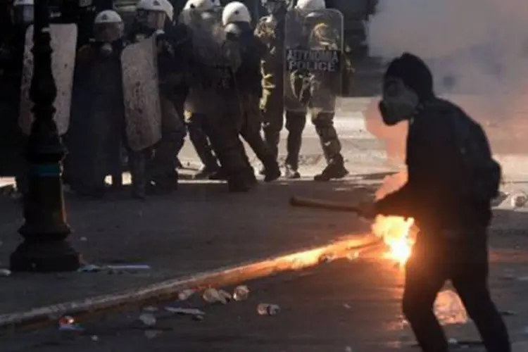 
	Manifestante enfrenta a pol&iacute;cia grega durante protestos em Atenas em 26 de setembro: alguns jovens tamb&eacute;m atearam fogo em lixeiras
 (Aris Messinis/AFP)