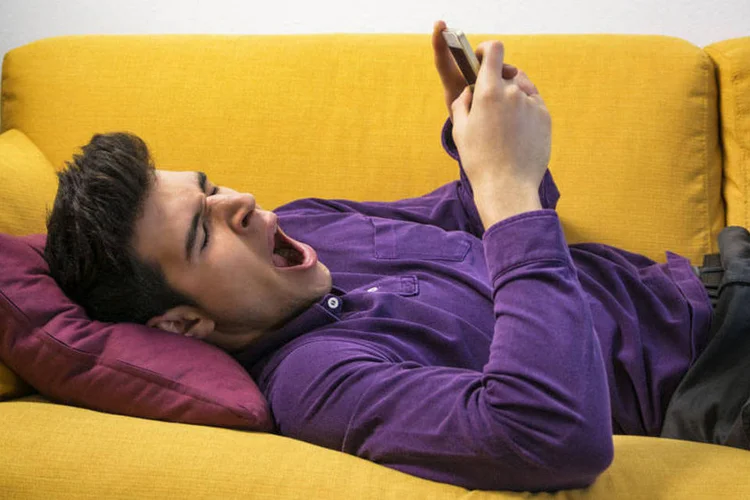 Homem deitado boceja enquanto usa celular (Thinkstock)