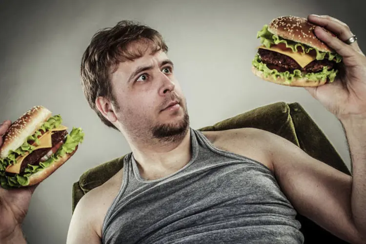
	Homem segura hamb&uacute;rgueres: fast food faz parte do consumo di&aacute;rio de calorias de crian&ccedil;as e adolescentes
 (Thinkstock)