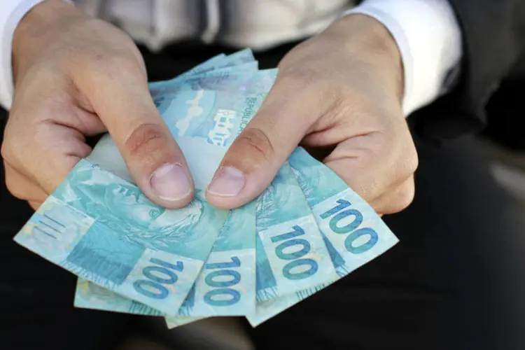 Homem segura notas de 100 reais (ThinkStock/Uelder Ferreira)