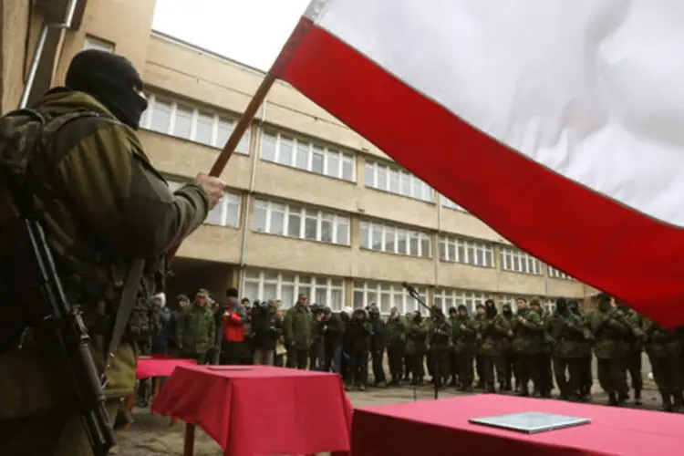 
	Homem segura uma bandeira da Crimeia enquanto membros de uma unidade pr&oacute;-R&uacute;ssia de autodefesa ficam em forma&ccedil;&atilde;o antes de dar um juramento ao governo da Crimeia, em Simferopol
 (Vasily Fedosenko/Reuters)