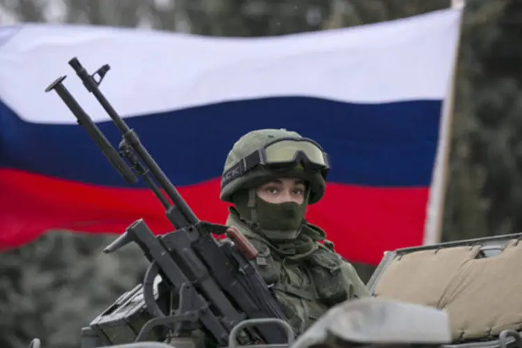 Um ativista pró-Rússia segura uma bandeira russa atrás de um militar armado no topo de um veículo do exército russo, próximo a um posto de controle de fronteira na cidade de Balaclava, na Crimeia (Baz Ratner/Reuters)