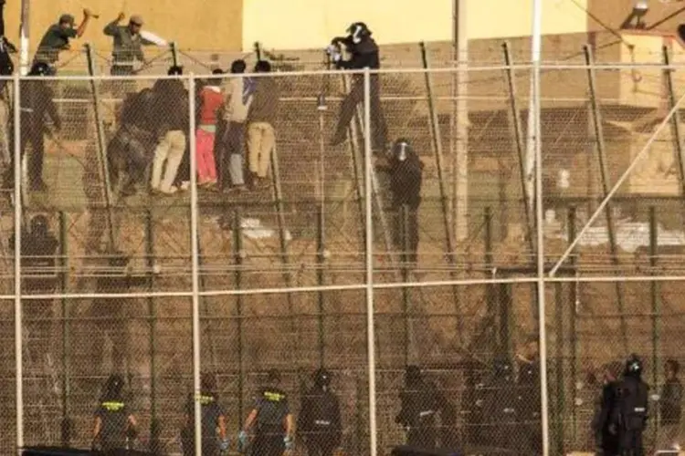 Membros da Guarda Civil espanhola observam dois integrantes das Forças Auxiliares marroquinas baterem em pessoas que tentam imigrar, escalando a tela que divide a África e a Espanha, no enclave de Melilla (Jose Colon/AFP)
