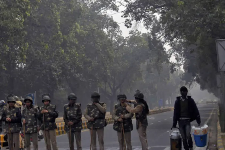 
	Vendedor de ch&aacute; passa por uma linha de policiais montando guarda em uma estrada de Nova Delhi:&nbsp;protestos se intensificaram rapidamente e se espalharam para outras cidades
 (Mansi Thapliyal/Reuters)