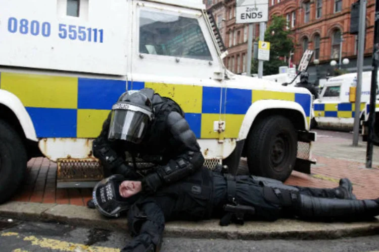 Policial socorre colega ferido durante confronto no centro de Belfast, na Irlanda do Norte (REUTERS/Cathal McNaughton)