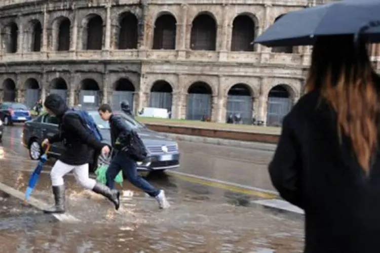 Pessoas tentam cruzar uma via inundada em frente ao Coliseu, em Roma  (Vincenzo Pinto/AFP)