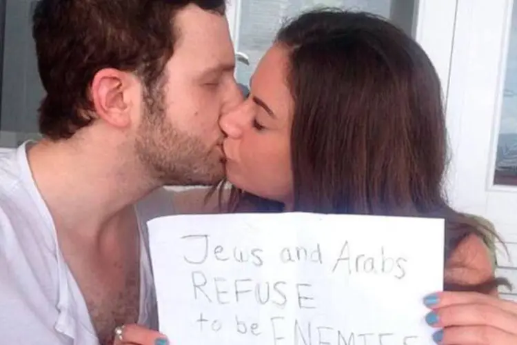 A libanesa Sulome Anderson e seu namorado, israelense, se beijam segurando uma folha que diz :"Judeus e árabes se negam a ser inimigos" (Reprodução/Twitter/Sulome Anderson)