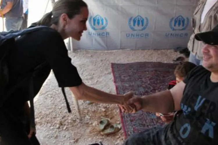 
	Angelina Jolie cumprimenta refugiado s&iacute;rio em campo na Jord&acirc;nia: a atriz, acompanhada por militares jordanianos, visitou as fam&iacute;lias que haviam acabado de chegar &agrave; fronteira
 (Khalil Mazraawi/AFP)