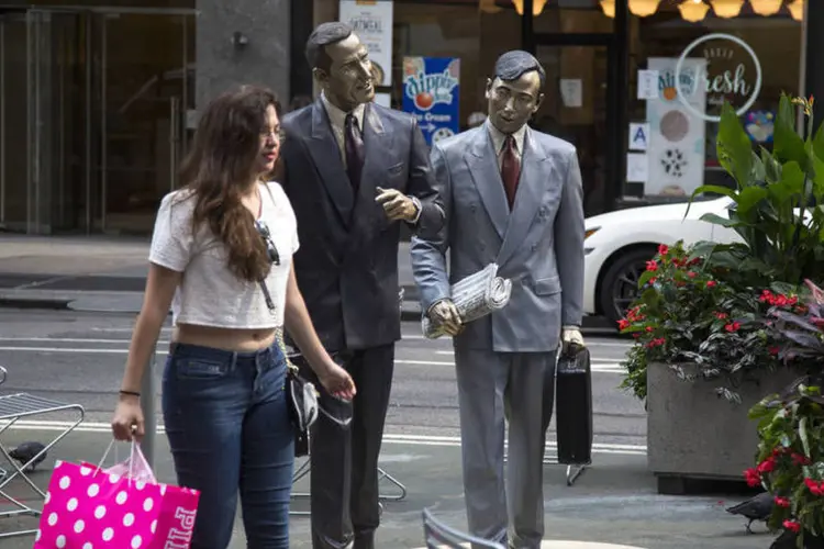Jovem caminha com sacola ao lado de uma escultura de Seward Johnson em Nova York, nos Estados Unidos (Michael Nagle/Bloomberg)