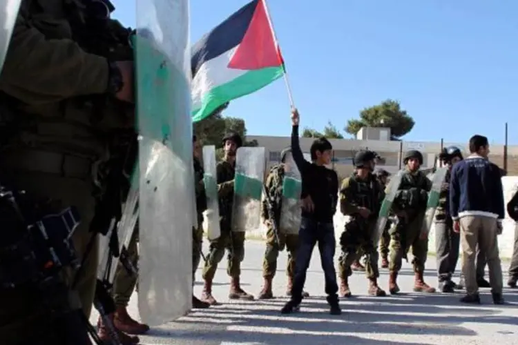 
	Jovem ergue bandeira da Palestina diante de militares de Israel: Israel j&aacute; criou cerca de 250 assentamentos.
 (Ammar Awad/Reuters)
