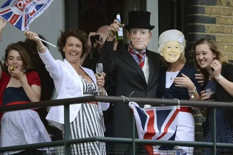 Espectadores usam máscara da rainha e do príncipe Philip, duque de Edimburgo, em varanda perto da Tower Bridge  (WPA Pool/ Getty Images)