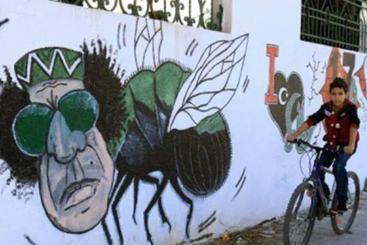 Criança passa por desenho do ex-ditador em muro na Líbia: Durda foi nomeado por Kadafi no início da revolta que eclodiu em 2011 para negociar com os rebeldes (Mahmud Turkia/AFP)