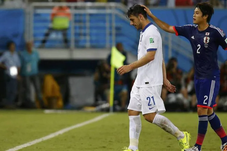 
	Jogador grego Kostas Katsouranis &eacute; consolado pelo japon&ecirc;s Atsuto Uchida depois de levar cart&atilde;o vermelho
 (Reuters/Kai Pfaffenbach)