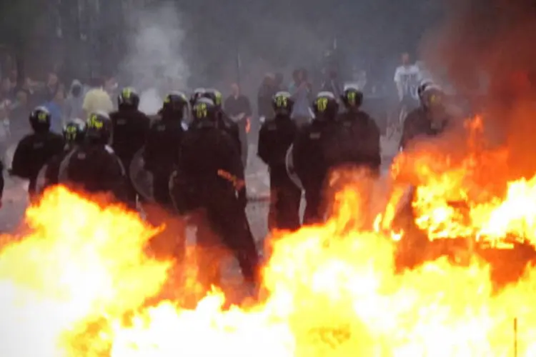 Policiais e manifestantes se enfrentam próximos a um carro em chamas em Hackney, Londres (Peter Macdiarmid/Getty Images)