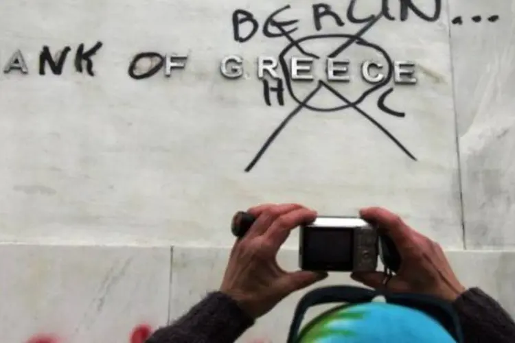 Pessoa fotografa pichação na fachada do Bank of Greece, que trocou o nome da instituição para "Bank of Berlin", em protesto (Milos Bicanski/Getty Images)