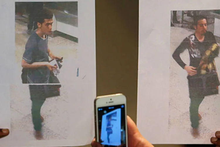 Policial segura foto de dois homens que, segundo as investigações, estavam viajando com passaportes roubados no avião desaparecido da Malaysia Airlines MH370 (REUTERS/Edgar Su)