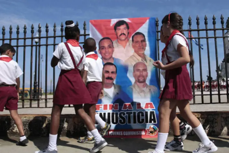 Crianças passam em frente a um cartaz com imagens dos cinco cubanos presos nos Estados Unidos, durante evento em apoio aos agentes em Havana (Reuters)