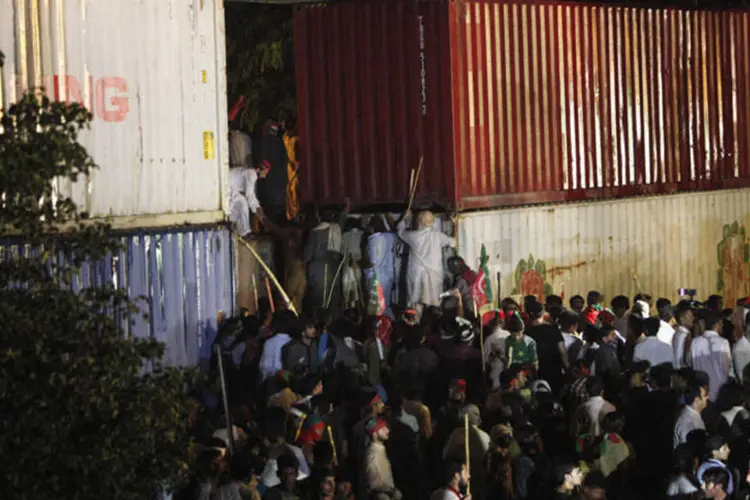 Manifestantes passam por barricada de contêineres no Paquistão (Akhtar Soomro/Reuters)