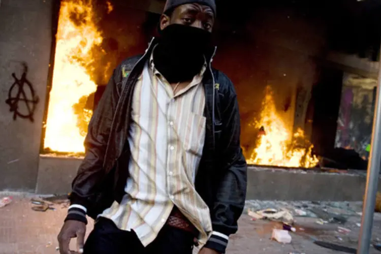 Manifestante mascarado passa em frende a Starbucks em chamas (David Ramos/ Getty Images)