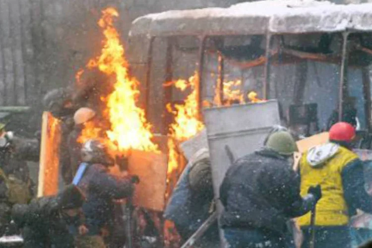 Manifestantes se protegem atrás dos destroços de um ônibus: polícia antidistúrbios lançou uma ofensiva na rua Grushevsky, perto da sede do governo (Sergei Supinsky/AFP)