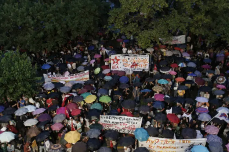 
	Manifestantes gregos protestam sob chuva do lado de fora da sede da TV estatal ERT, em Atenas: o governo anunciou ontem o fim da ERT
 (REUTERS / John Kolesidis)