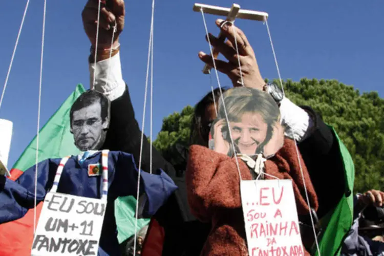 
	Um manifestante brinca com fantoches que representam o primeiro-ministro de Portugal, Pedro Passos Coelho (e) e a chanceler alem&atilde;, Angela Merkel
 (Hugo Correia/Reuters)