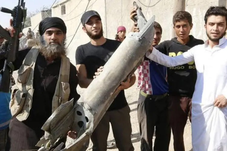 Militante do Estado Islâmico segura peça de avião militar sírio ao lado de moradores de Raqqa, no norte da Síria (Reuters)