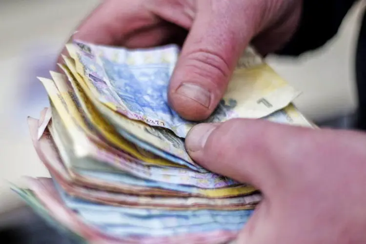 
	Comerciante segura notas de gr&iacute;vnia, a moeda ucraniana, em Kiev: acordo permite que Kiev obtenha mais de US$ 3 bilh&otilde;es em ajuda do FMI nos pr&oacute;ximos dias
 (Vincent Mundy/Bloomberg)