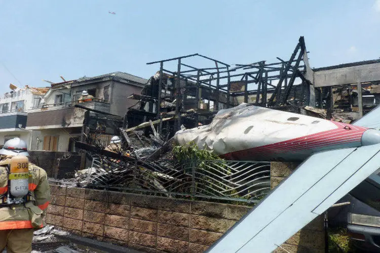 
	Bombeiro ao lado do monomotor que caiu em Chofu, T&oacute;quio: casas e carros foram incendiados, tr&ecirc;s pessoas morreram e cinco ficaram feridas
 (REUTERS/Kyodo)