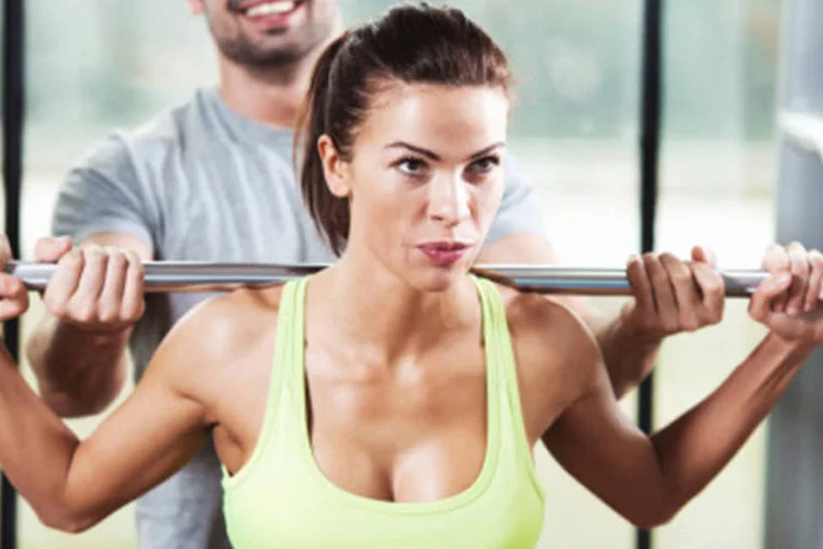 Mulher levantando peso na academia: exercícios de alongamento também podem ser feitos durante o treinamento de força, como intermédio entre um exercício e outro, conforme a sua necessidade (Getty Images)