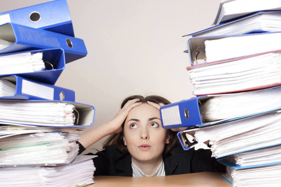 Mulher cansada com uma pilha de documentos (Thinkstock)