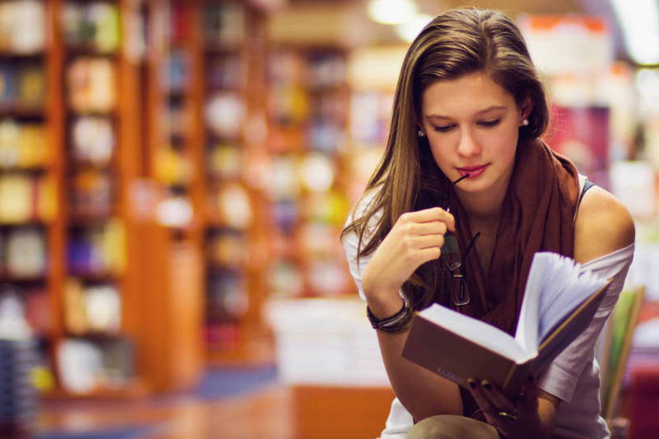 Mulher lendo livro em biblioteca (Thinkstock)