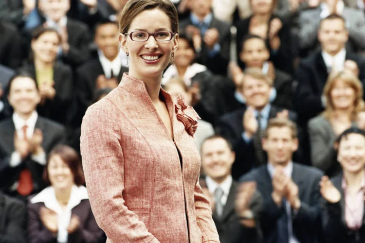 Mulher sorri em frente a grupo de executivos (Thinkstock)
