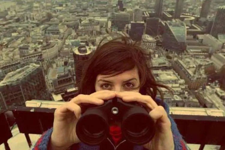Mulher usa binóculo com cidade ao fundo (Getty Images)