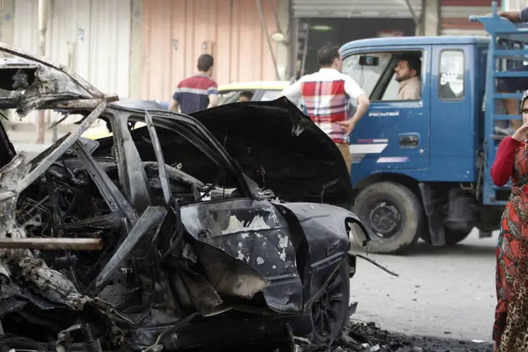 Mulher observa veículo destruído ao passar pelo local onde houve um ataque a bomba, no distrito de Al-Mashtal, em Bagdá (REUTERS/Thaier Al-Sudani)