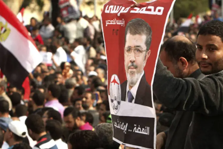 Apoiador do presidente egípcio Mohamed Mursi carrega poster com imagem de Mursi, enquanto outros cantam slogans pró-Mursi durante manifestação em frente ao Palácio Presidencial no Cairo (Asmaa Waguih/Reuters)