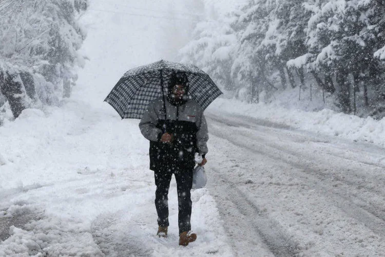 Homem segura guarda-chuva e caminha durante nevasca em villarejo do Líbano (Mohamed Azakir/Reuters)