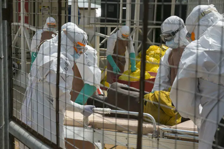 Profissionais britânicos transferem um recém-internado paciente com ebola para maca, em Freetown (Baz Ratner/Reuters)