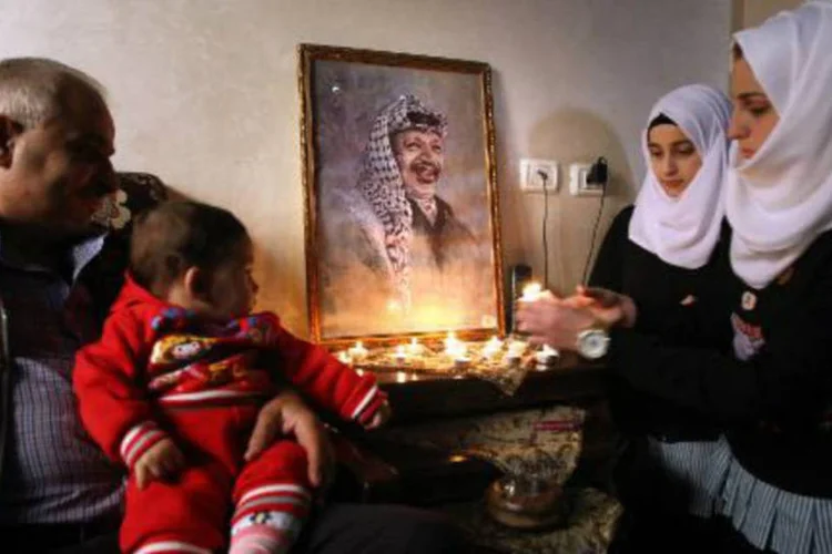 
	Fam&iacute;lia palestina acende velas em frente a retrato do l&iacute;der da Autoridade Palestina Yasser Arafat
 (Hazem Bader/AFP)