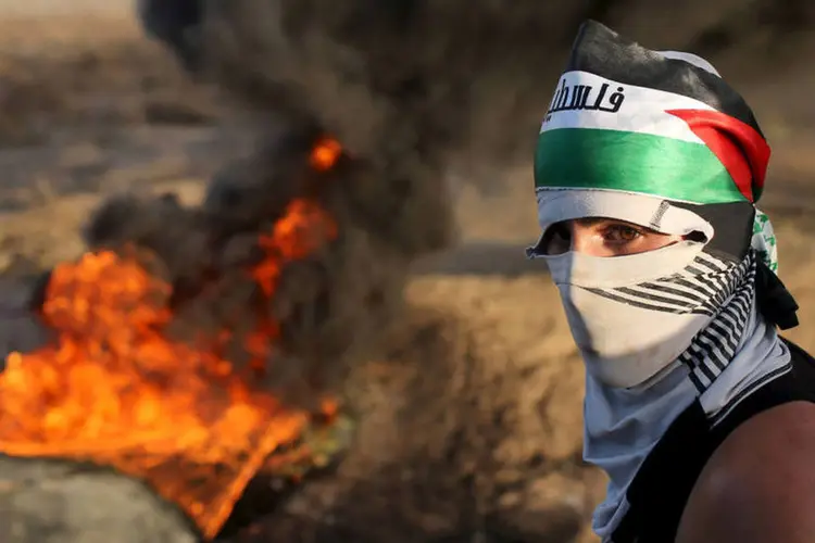 
	Palestino em frente a pneus em chama em protesto na Cisjord&acirc;nia: a agress&atilde;o &eacute; parte de uma onda de viol&ecirc;ncia que j&aacute; resultou na morte de cerca de 60 pessoas
 (Reuters / Ibraheem Abu Mustafa)