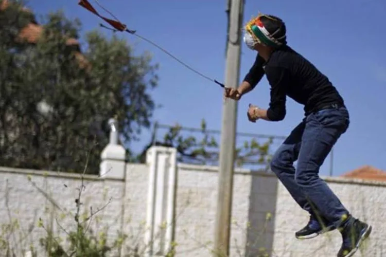 
	Palestino usa um estilingue para atirar uma pedra em dire&ccedil;&atilde;o a soldados israelenses: manifesta&ccedil;&otilde;es motivaram projeto
 (REUTERS/Mohamad Torokman)