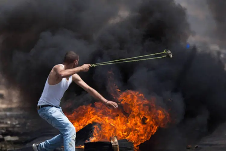 Palestino protesta ao lado de pneus queimados contra a ocupação israelense (Uriel Sinai/ Getty Images)