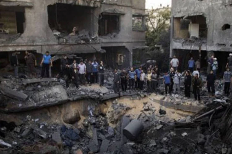 
	Palestinos ao redor de cratera causada por ataque israelense na Cidade de Gaza: o ex&eacute;rcito israelense realizou mais de 1.350 ataques contra alvos em Gaza
 (Marco Longari/AFP)
