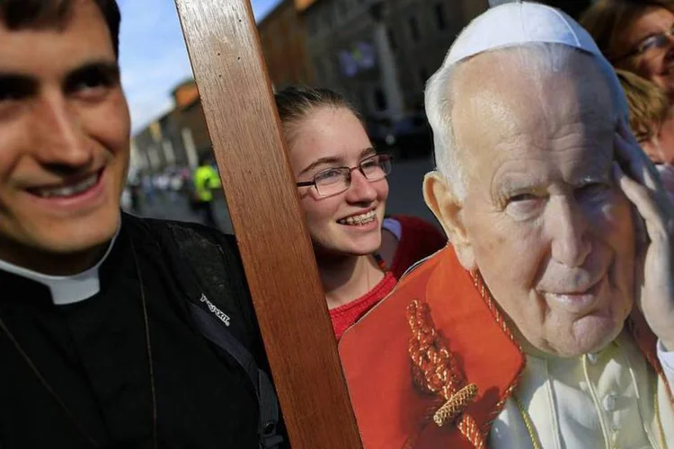 Fiéis tiram fotos com a imagem do papa João Paulo II em frente a praça de São Pedro, em Roma (Tony Gentile/Reuters)