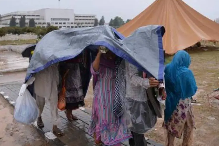 Paquistaneses usam uma lona para se proteger da chuva que atinge o país (Aamir Qureshi/AFP)