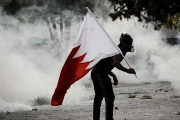 Homem protesta com a bandeira do Bahrein e se protege do gás lacrimogênio: país registra distúrbios desde fevereiro de 2011 (Mohammed Al-Shaikh/AFP)